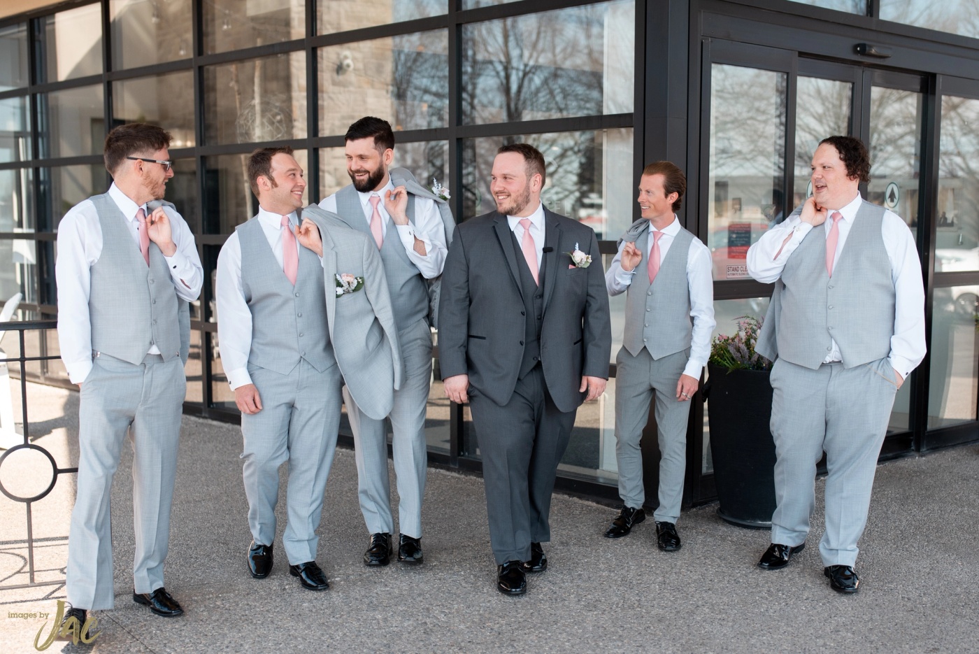 Groomsmen in pale blue suits adjust their ties outside a glass-fronted venue