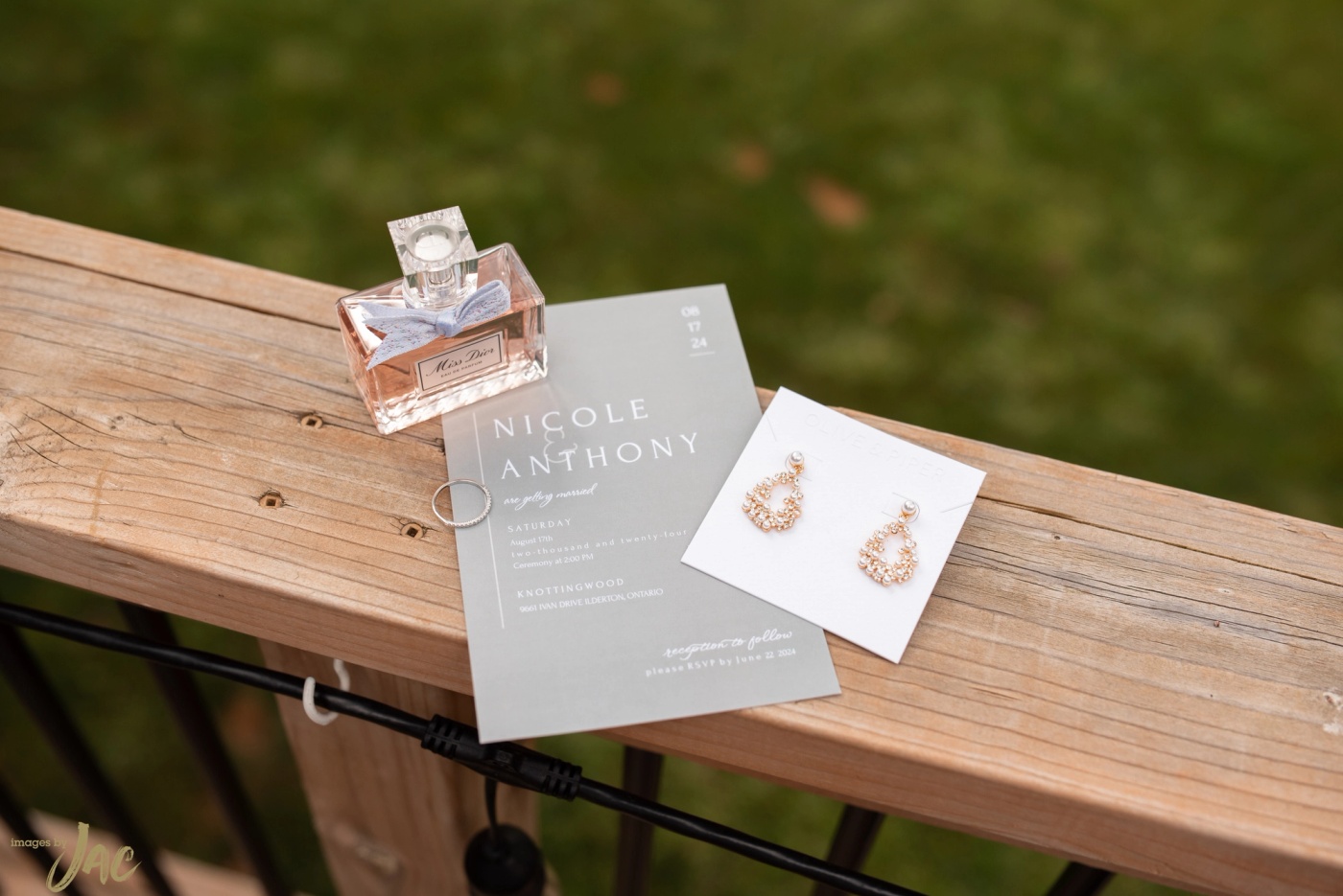 A wedding invitation for Nicole and Anthony with perfume and earrings on a wooden bench