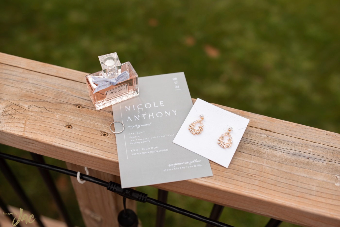 A wedding invitation for Nicole and Anthony with perfume and earrings on a wooden bench