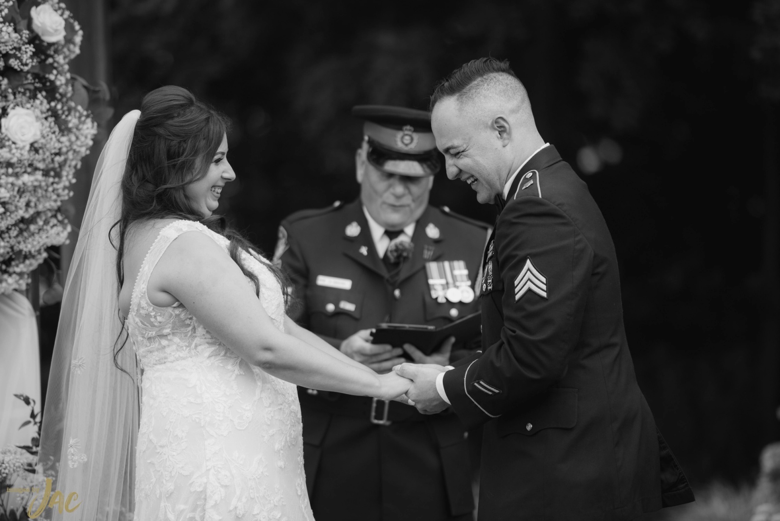 A bride and her groom in military dress uniform laughing as they hold hands during their outdoor ceremony