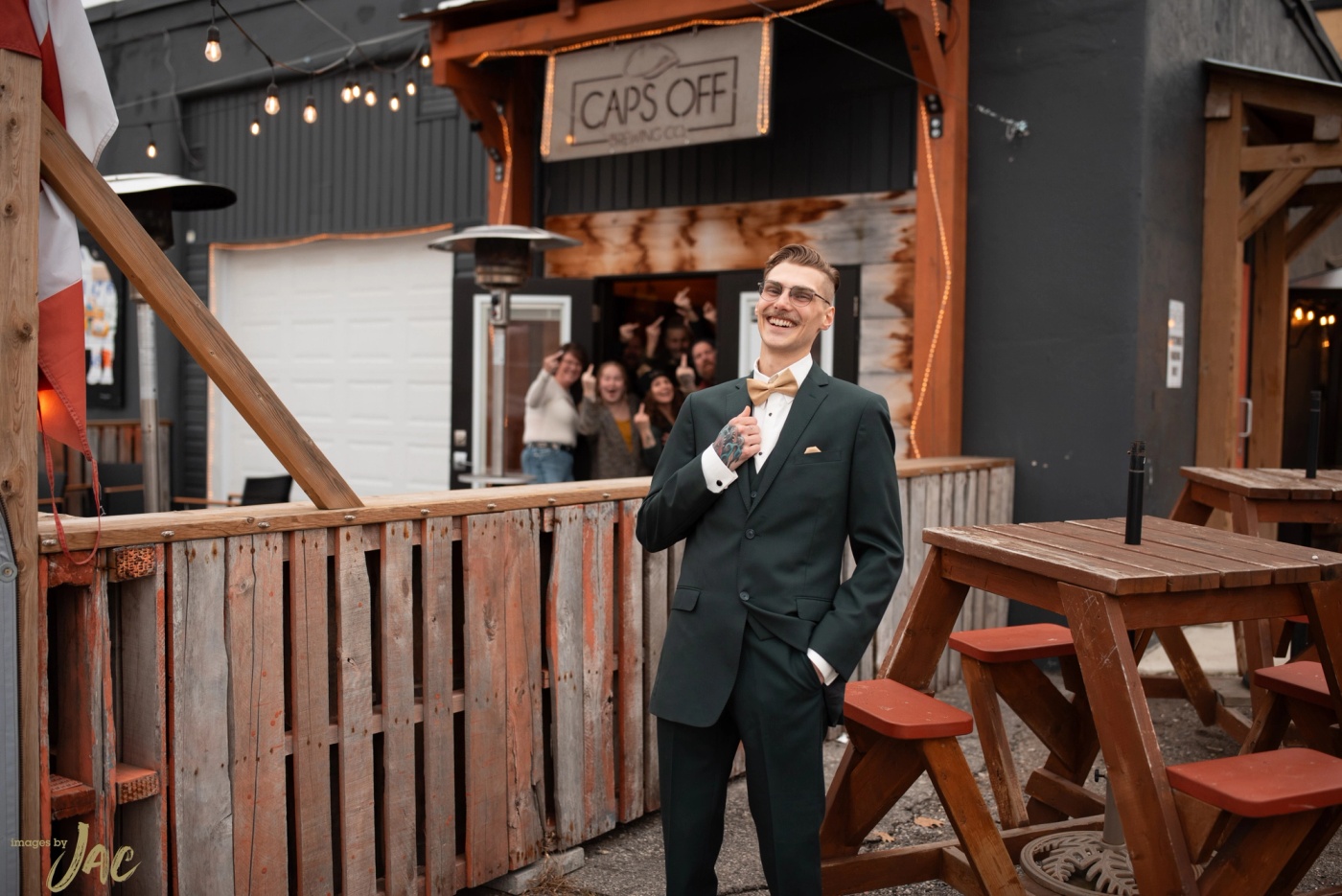 A groom in a dark green suit outside a bar, hands in his pockets