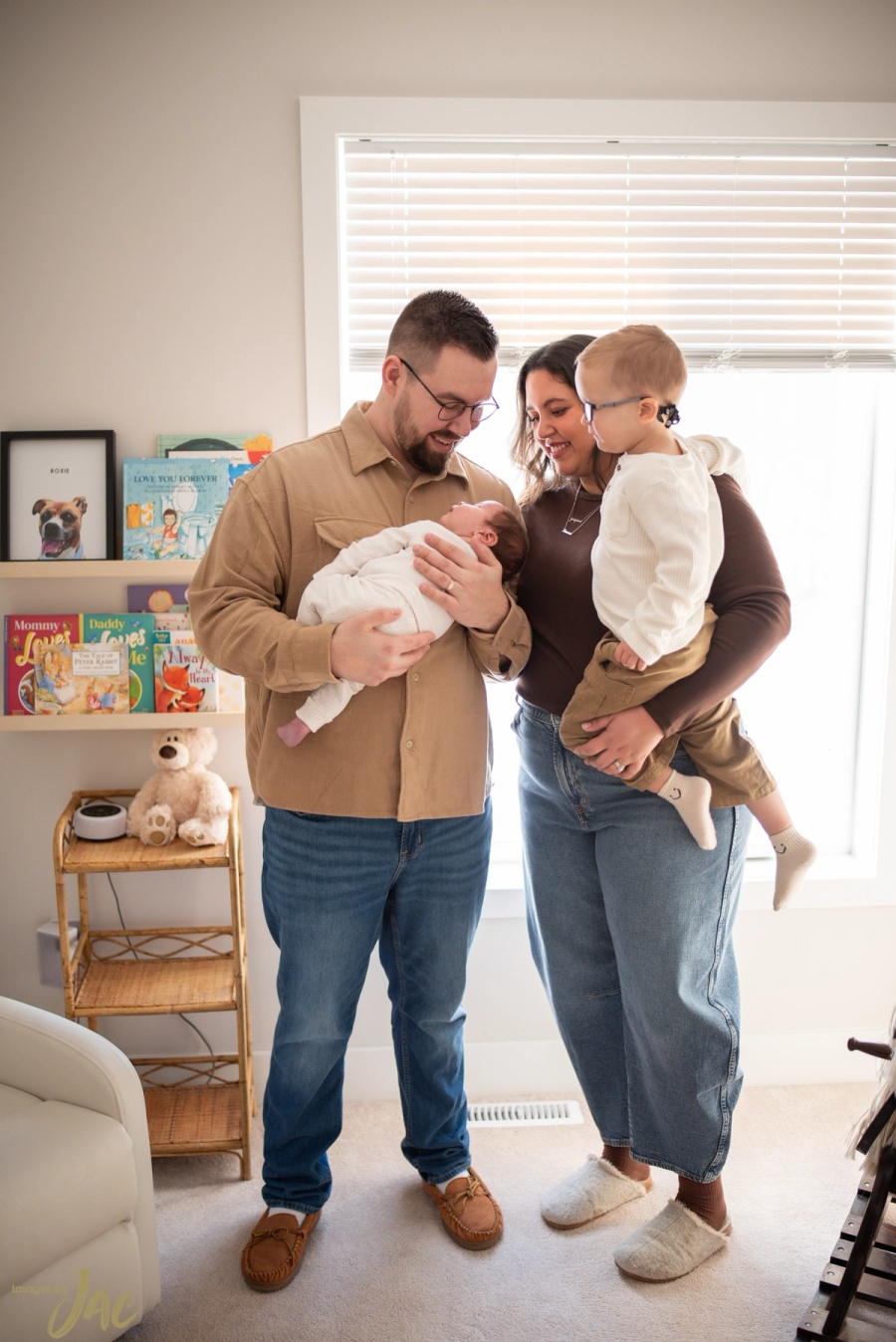 Parents hold their newborn and toddler in a bright living room