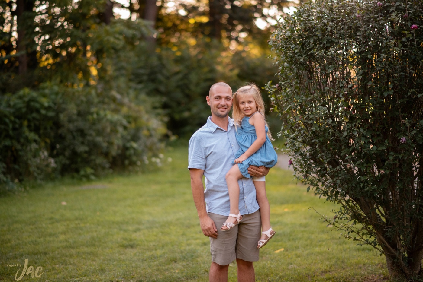 A father carries his young daughter along a garden path at sunset