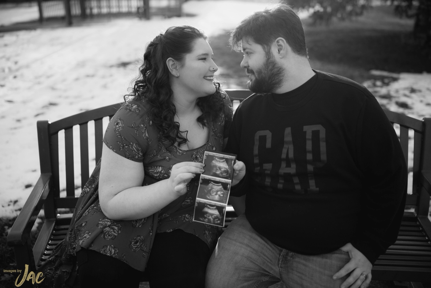 A couple sit on a bench in the snow holding an ultrasound photograph