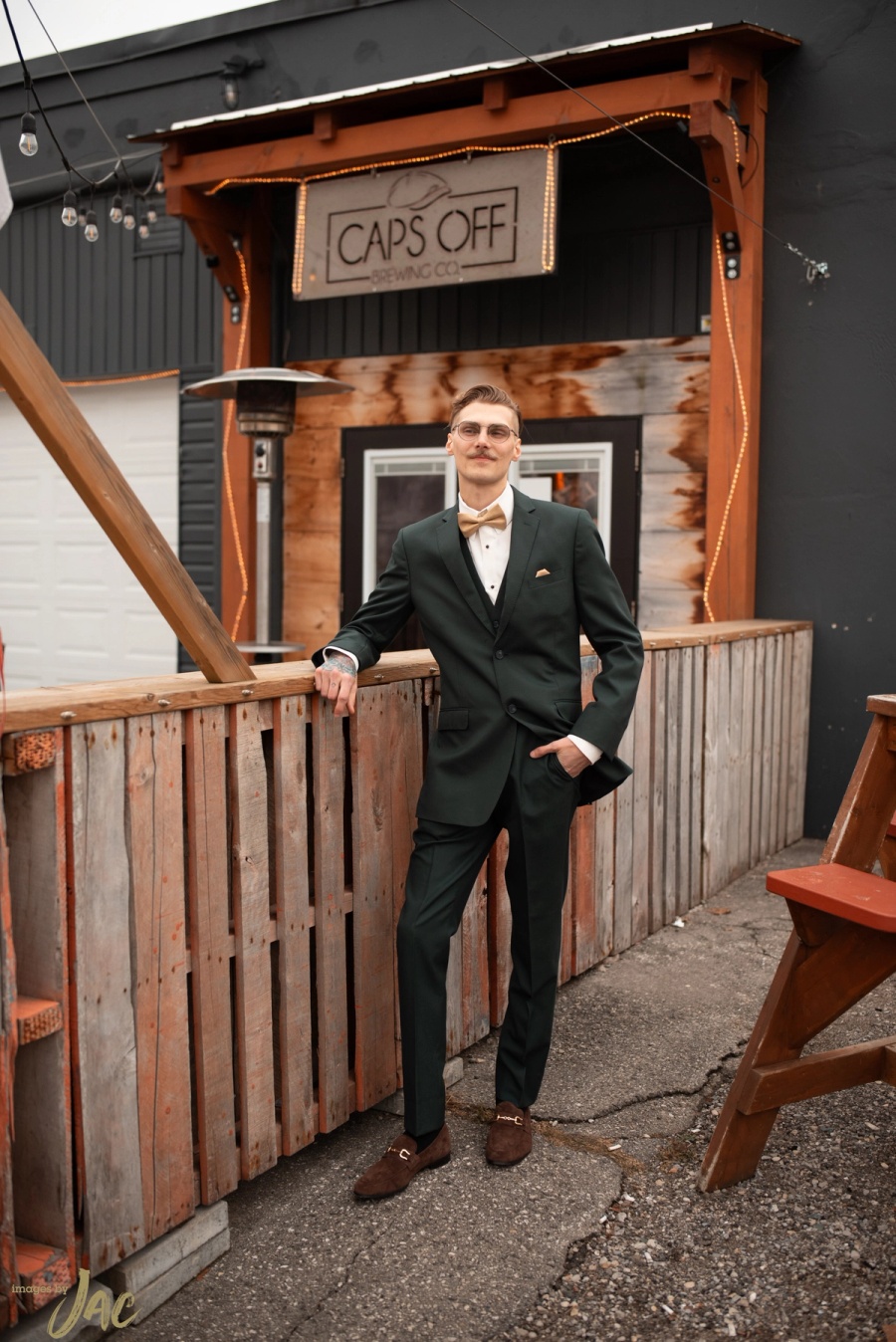A groom in a dark green suit leaning on a railing outside a bar