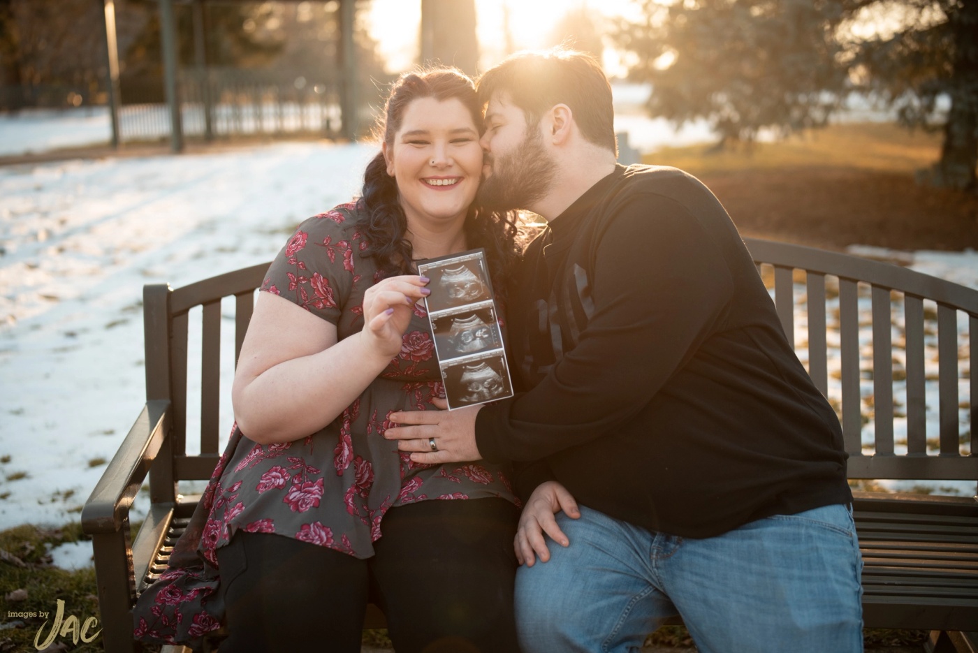 A couple sit on a snowy bench holding an ultrasound photograph
