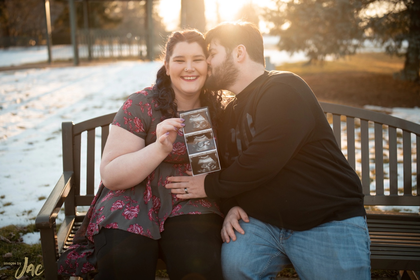 A couple sit on a snowy bench holding an ultrasound photograph