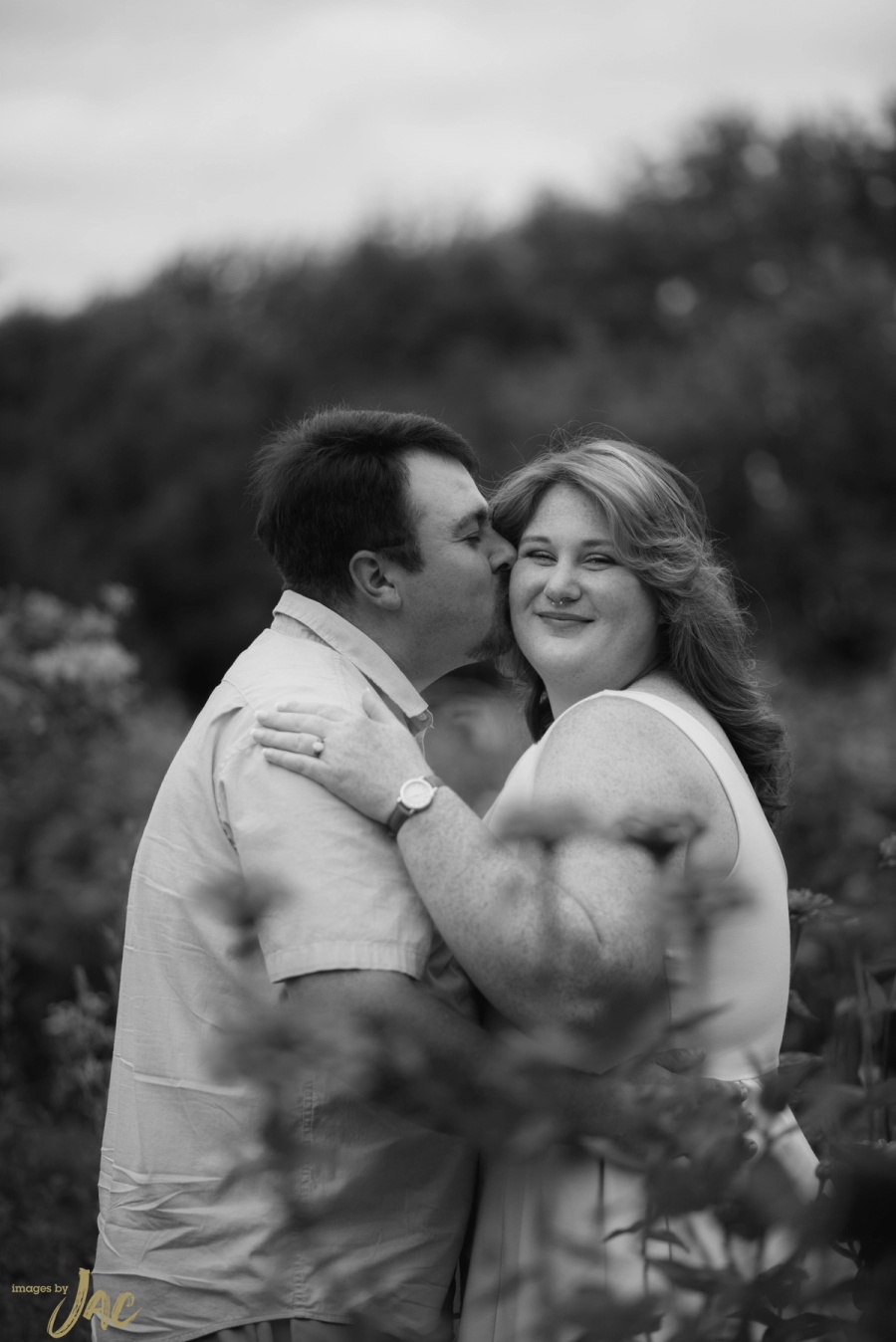 A man kisses his partner's cheek in a field of tall flowers