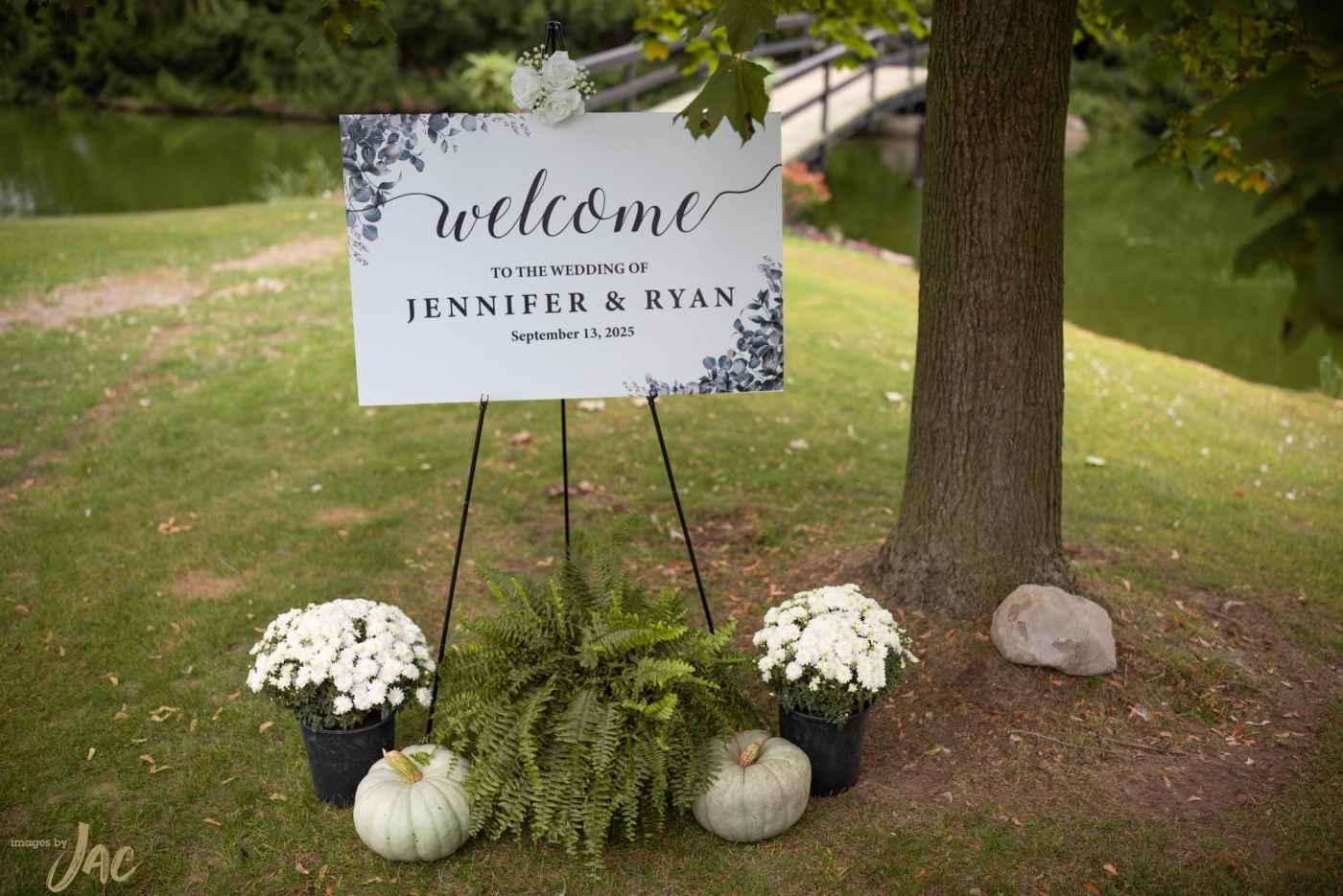 A welcome sign for Jennifer and Ryan's wedding on an easel, framed by white mums, ferns and pale pumpkins