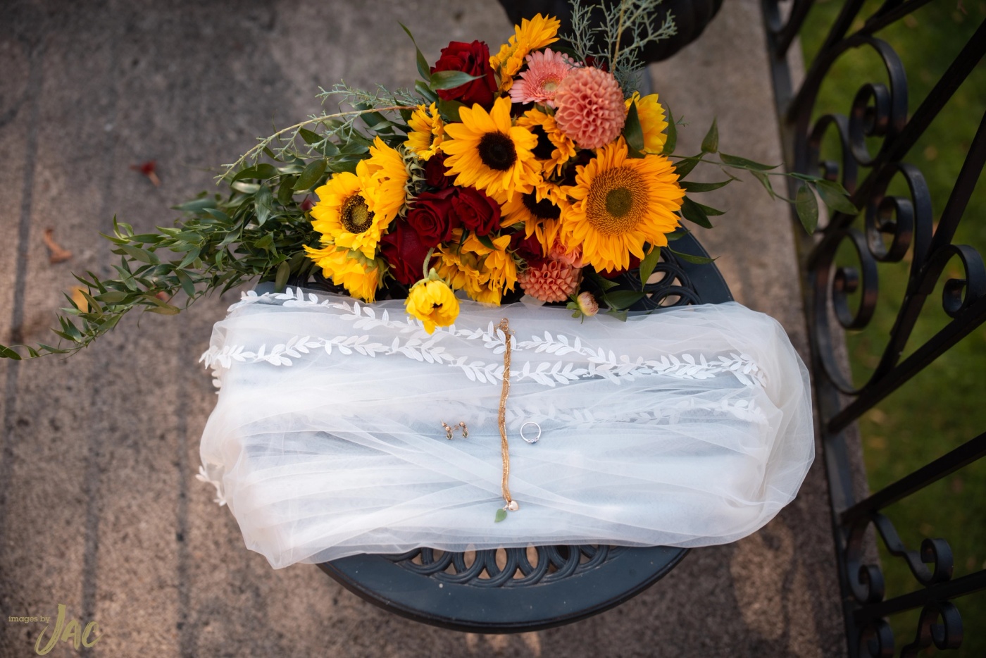A bouquet of sunflowers and dahlias resting on a bench beside a folded veil