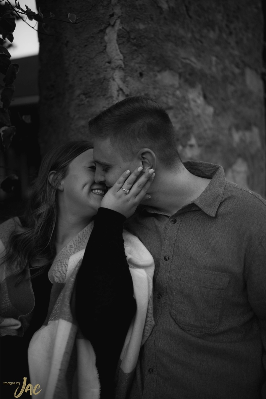 A couple laugh forehead to forehead against a stone wall