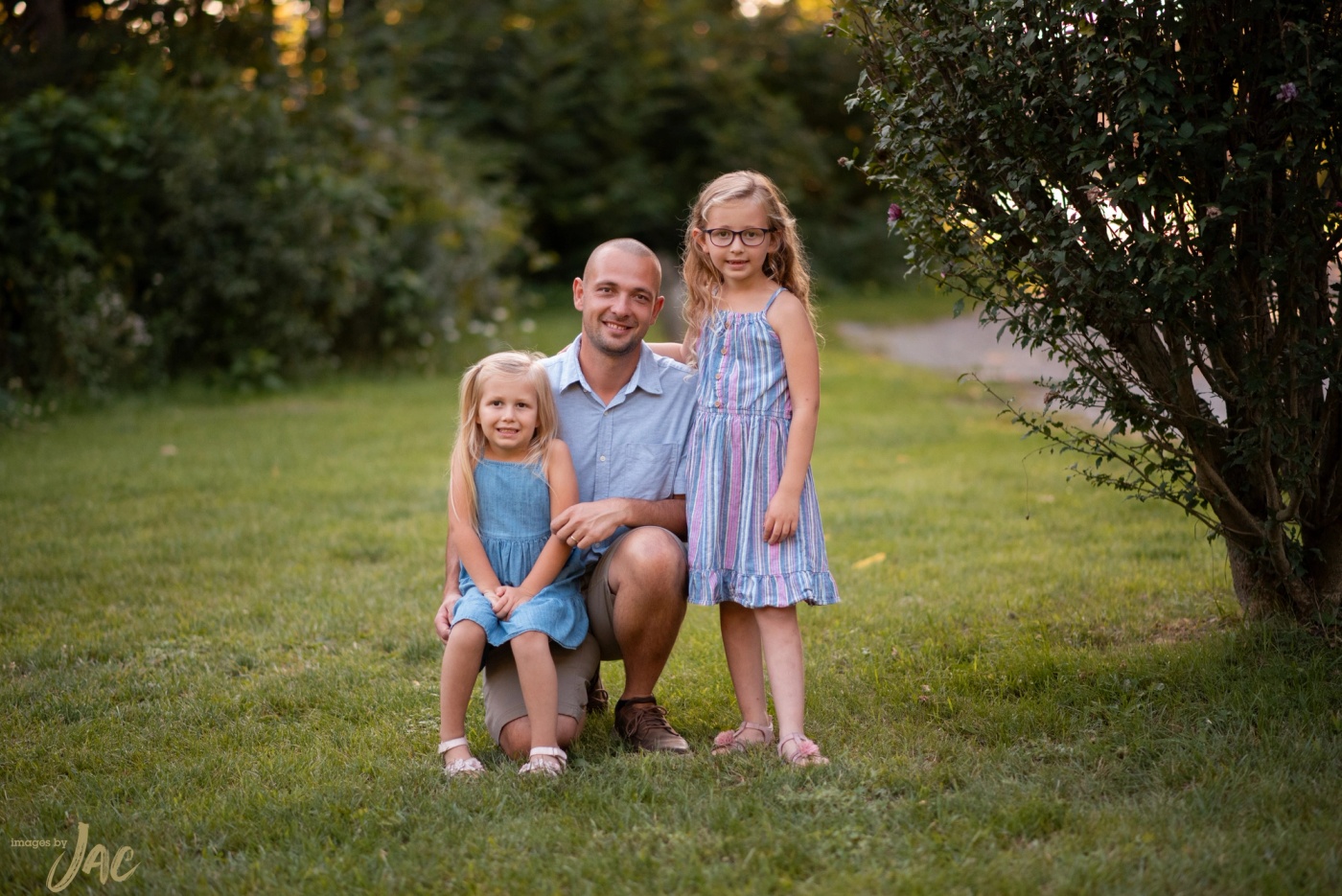 A father kneels on the grass between his two young daughters