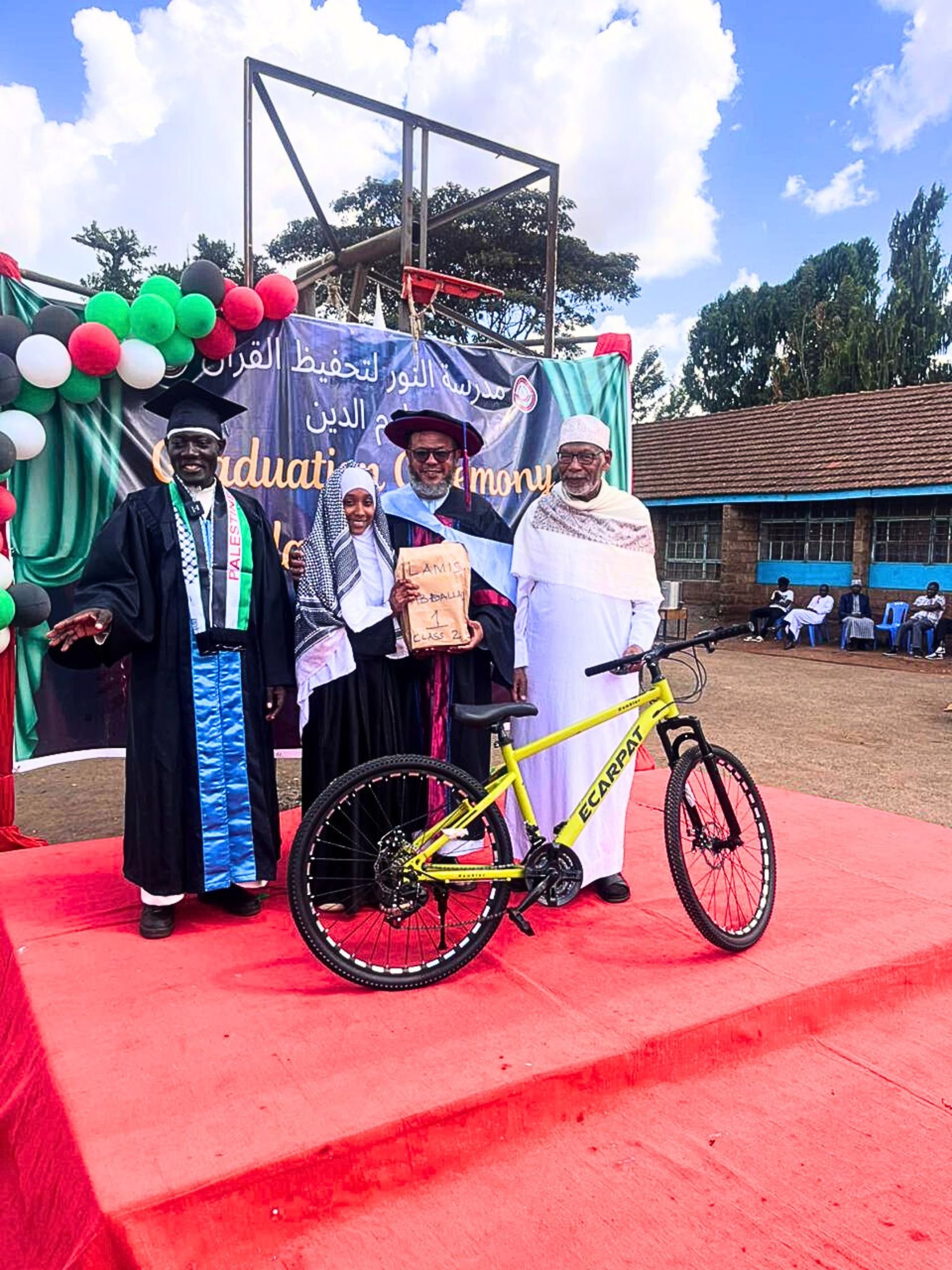 Lamis Abdallah being presented a bicycle as a reward for her splendid performance by Sheikh Ahmad Uthman. Five top learners at the madrasa were awarded bicycles and other prizes to recognize their performance. On the left is a teacher at the madrasa Abdulrahman Jaffar and right is Prof. Mohammed Bakari