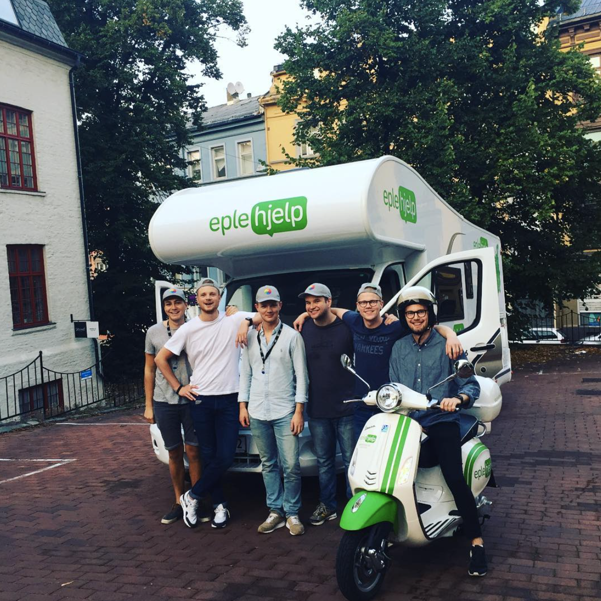 Seks menn poser foran en bobil og en scooter merket "eple hjelp".