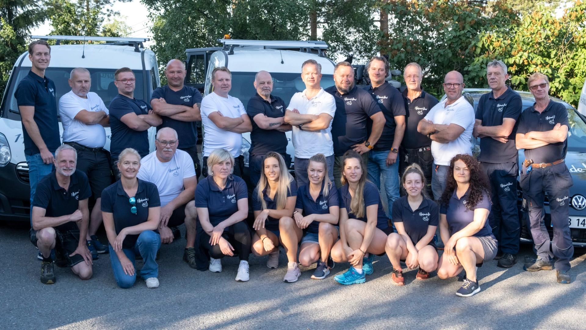 En gruppe smilende vaktmestere og ansatte poserer foran en flåte av servicebiler.