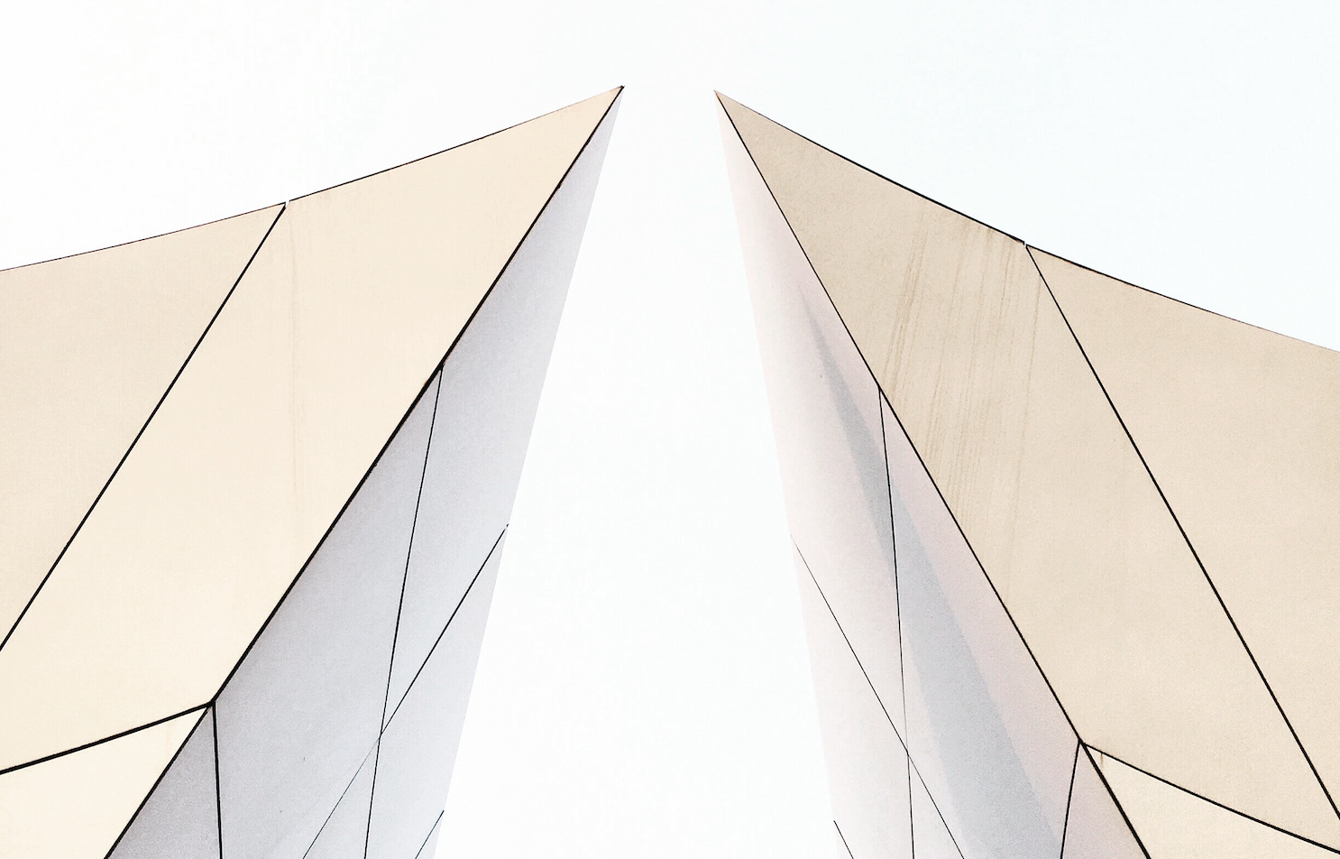 Abstrakt bilde av to bygningsstrukturer i lyse farger som peker oppover mot en hvit himmel.