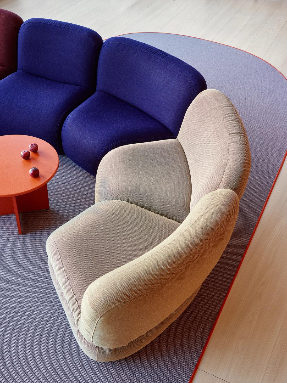 Stue med en blå sofa, beige lenestol, oransje bord med plommer, og et lilla teppe på et tregulv.