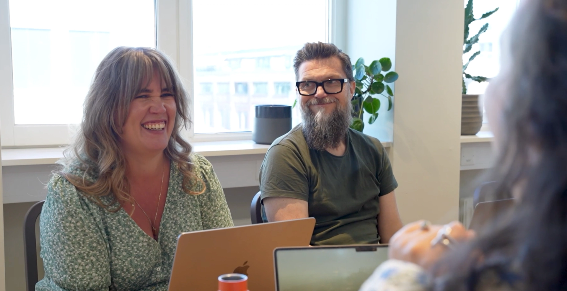 To smilende kolleger ser på en tredje person, med bærbare datamaskiner foran seg.