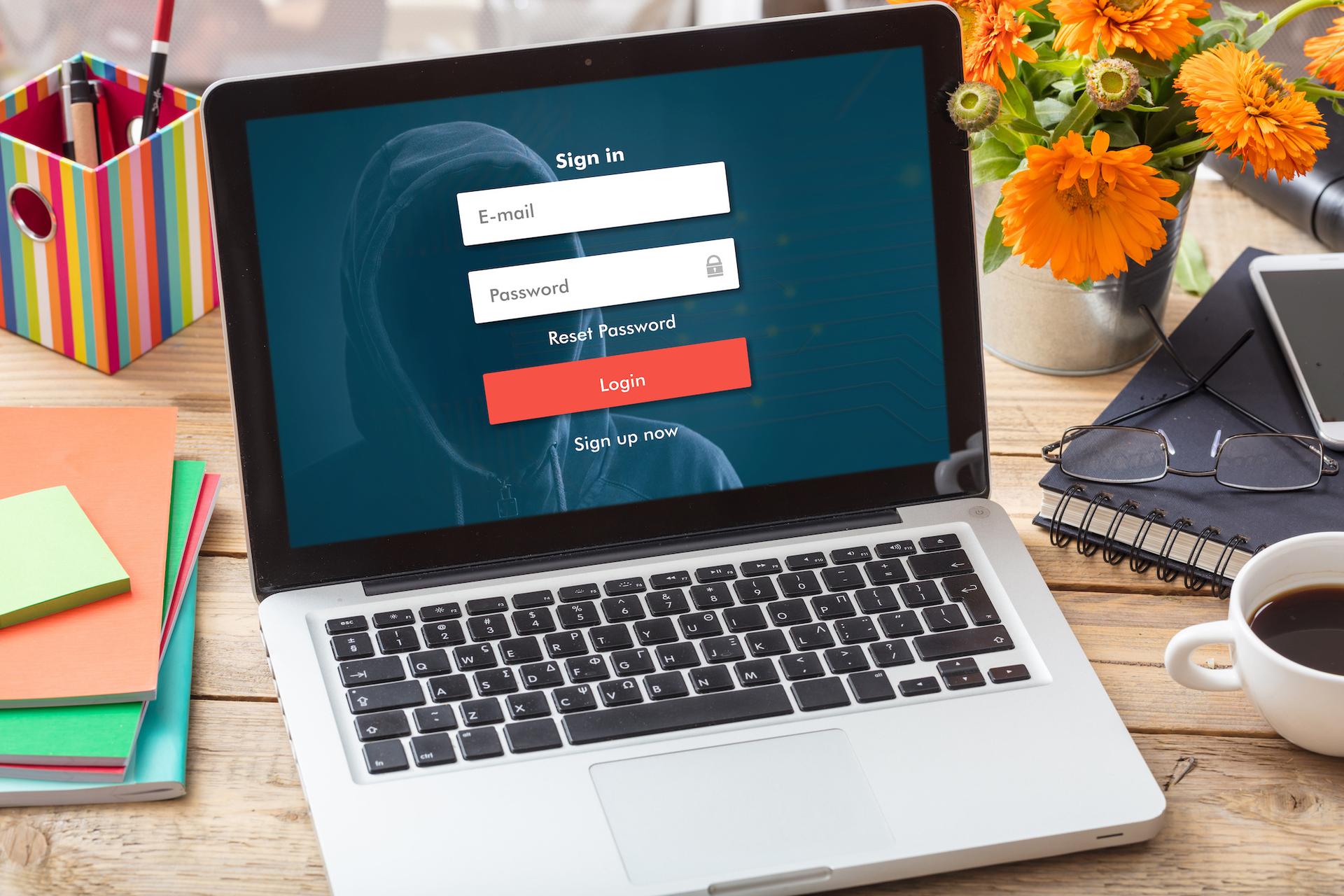 Bærbar datamaskin viser en innloggingsside med en person i hettegenser i bakgrunnen, omgitt av kontorrekvisita.