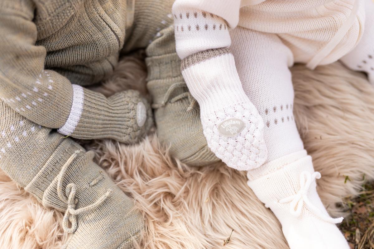 Et nærbilde av to babyer kledd i Lillelam-klær, liggende på et lunt teppe, den ene i grønt og den andre i hvitt.