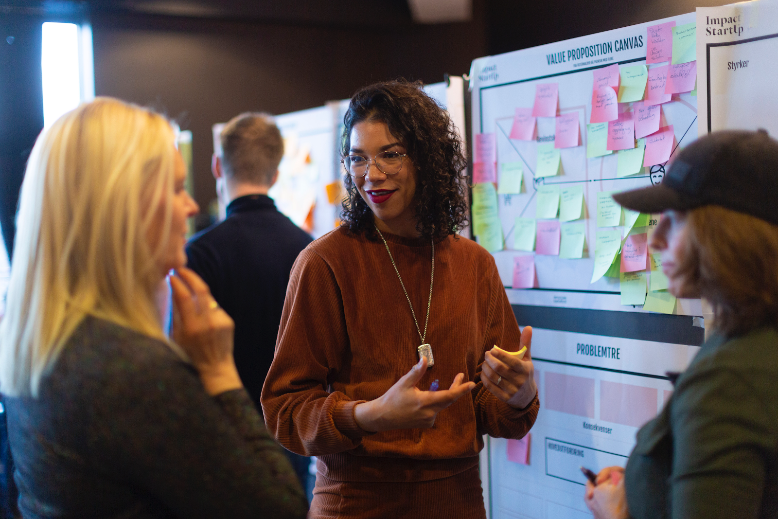 Tre personer diskuterer foran en tavle med post-it-lapper under en Impact StartUp workshop.