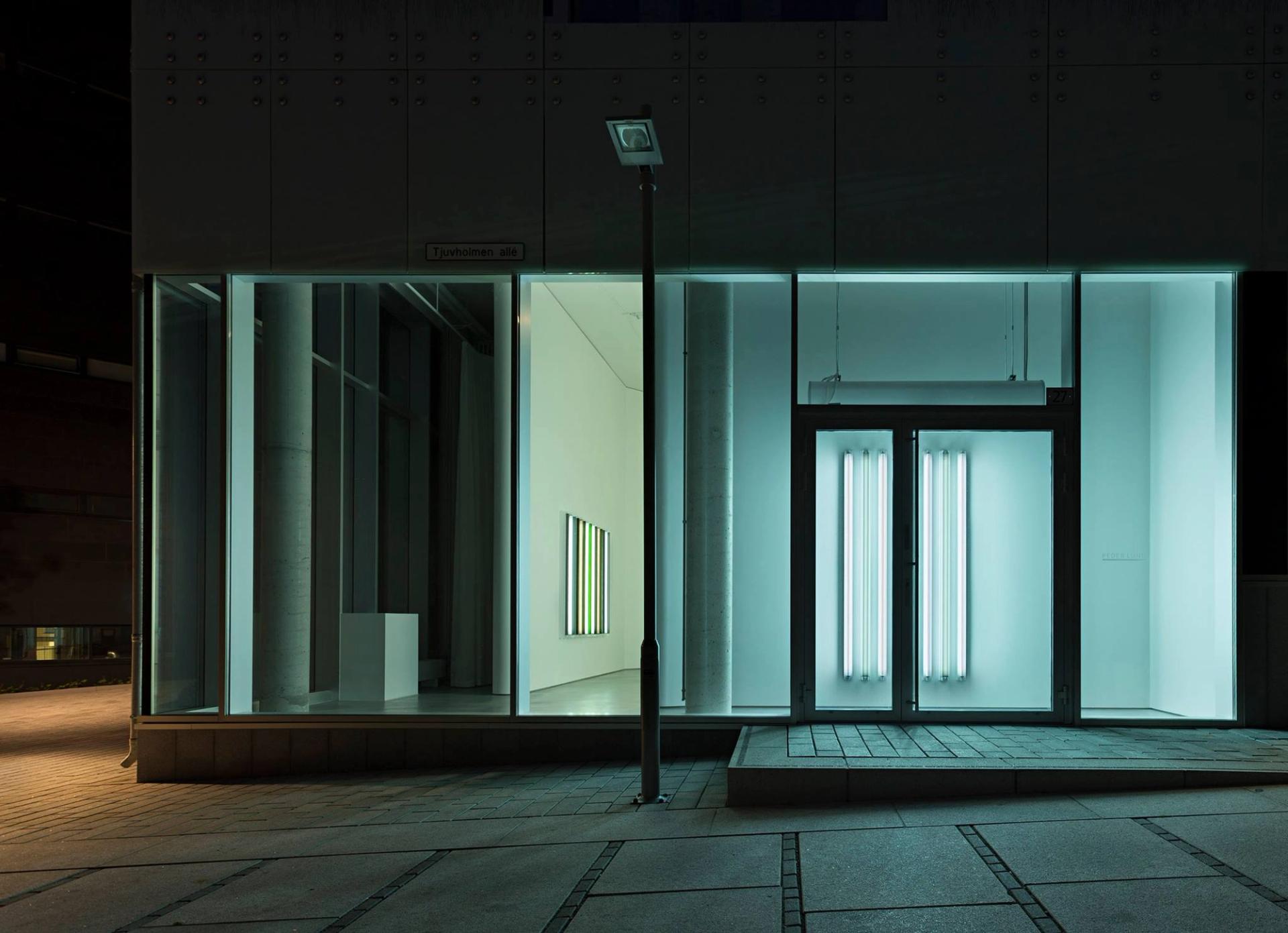 Et gatebilde om natten viser en moderne bygning med store vinduer og neonlys, beliggende på "Tjuvholmen allé".