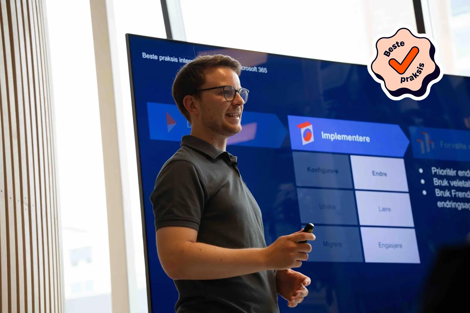 Mann presenterer en "Beste praksis" slide på en skjerm med teksten "Implementere" og "Forvalte" med tilhørende underpunkter.