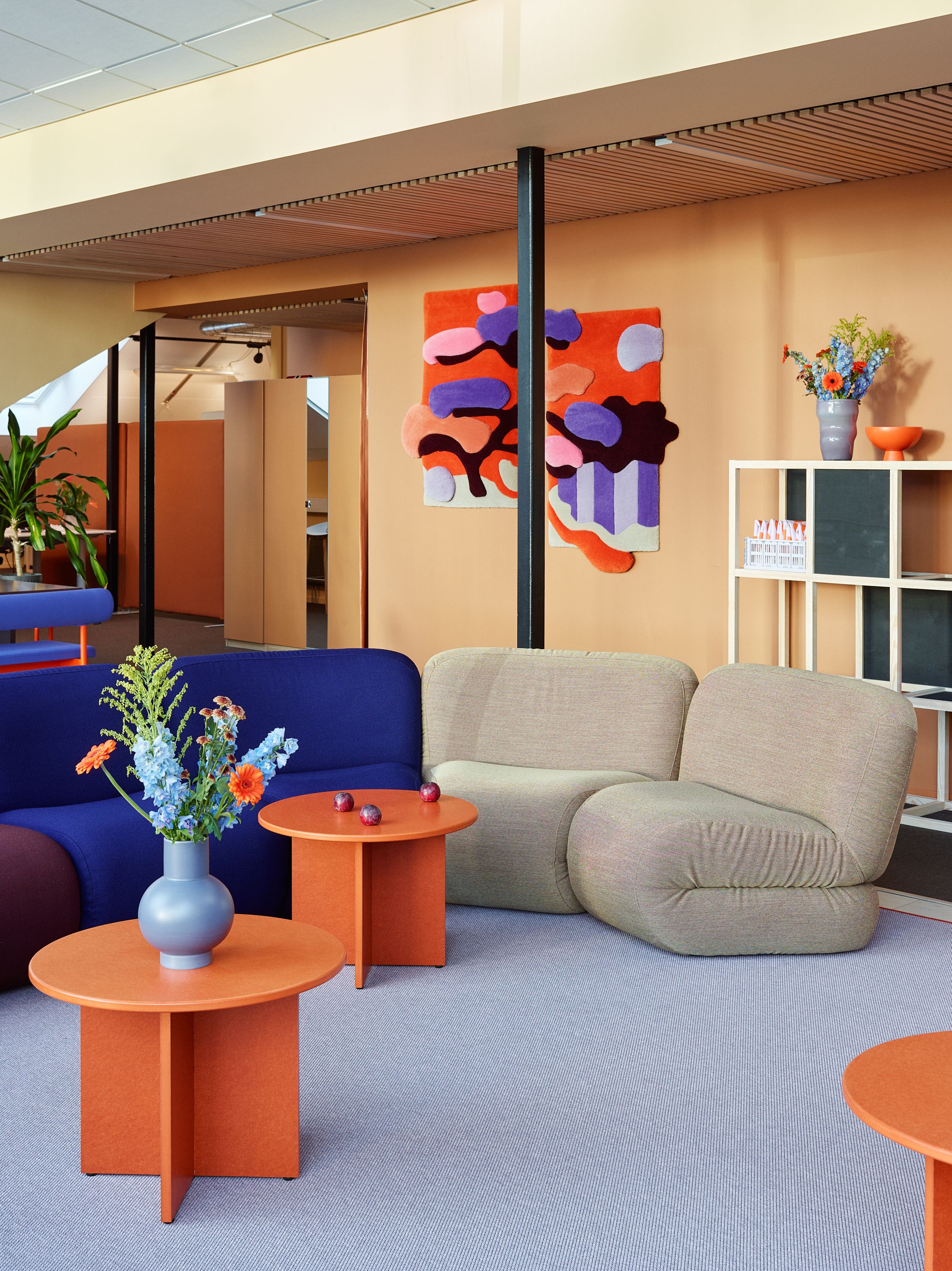 Fargerikt kontorinteriør med blå sofa, lysegrå stoler, oransje sidebord og en stripet veggdekorasjon.