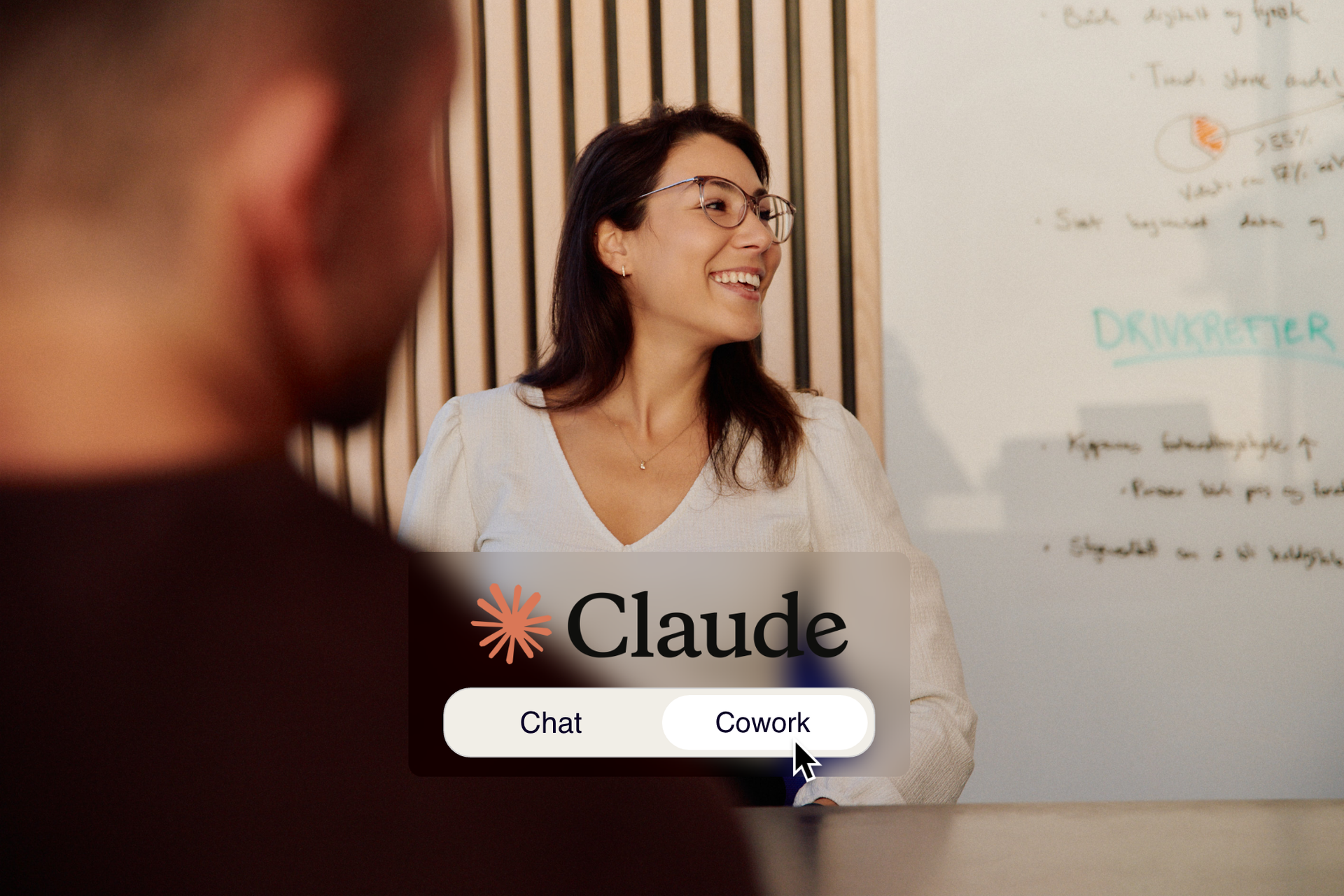 Smilende kvinne med briller og en mann i samtale foran en tavle med tekst, med grensesnitt for Claude overlagt i forgrunnen