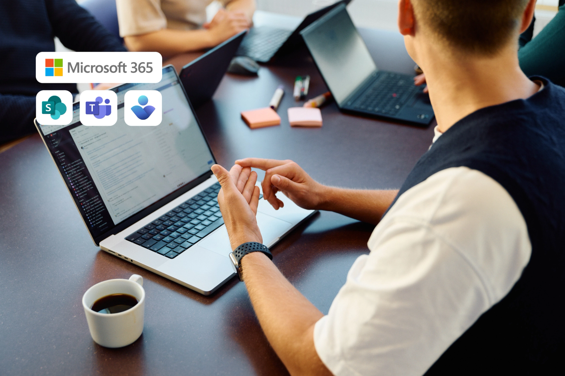 En person bruker en laptop med Microsoft 365-ikoner for SharePoint, Teams og en ukjent app, mens andre sitter rundt et bord.