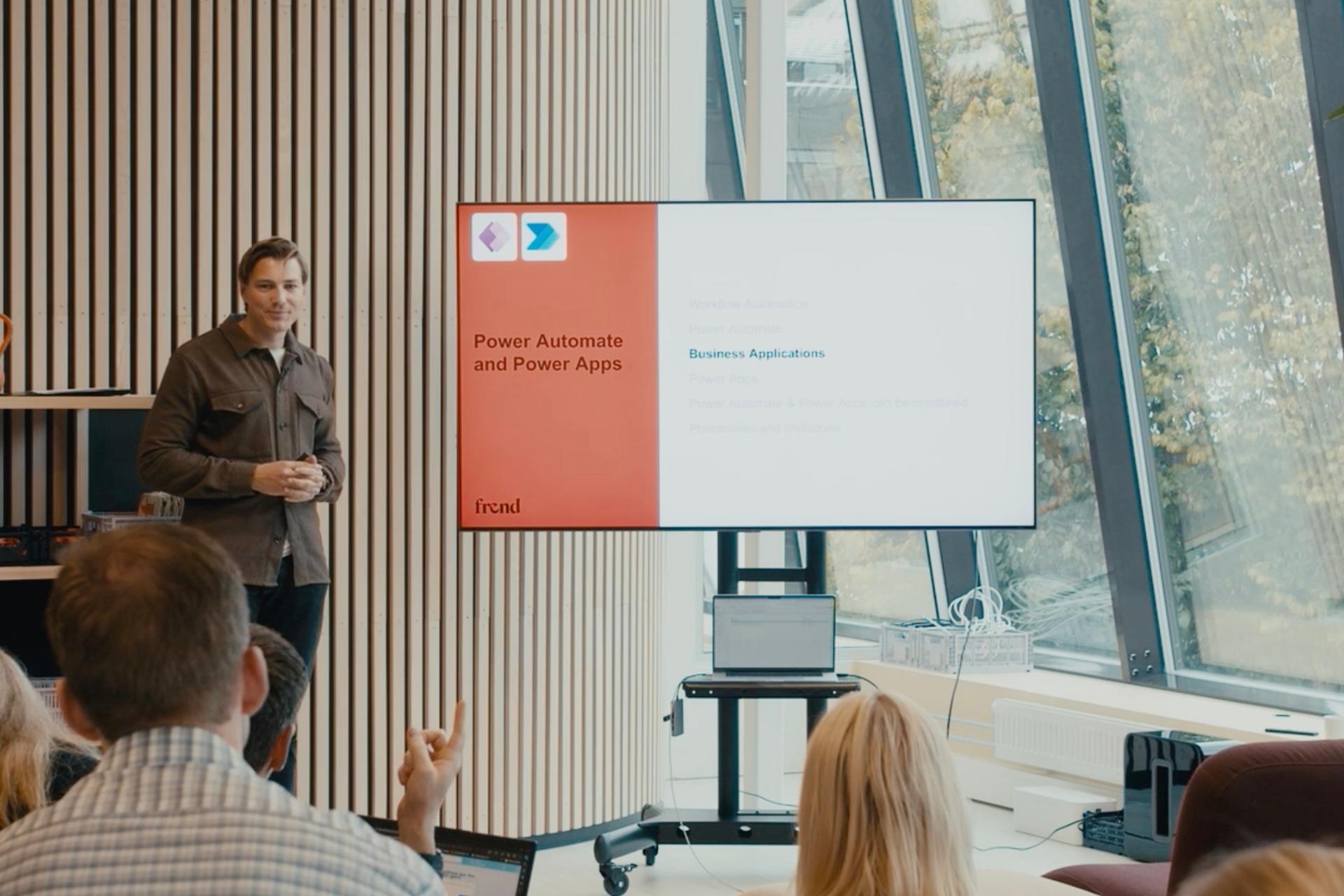 En foreleser presenterer Power Automate og Power Apps på en skjerm foran et publikum på et seminar.