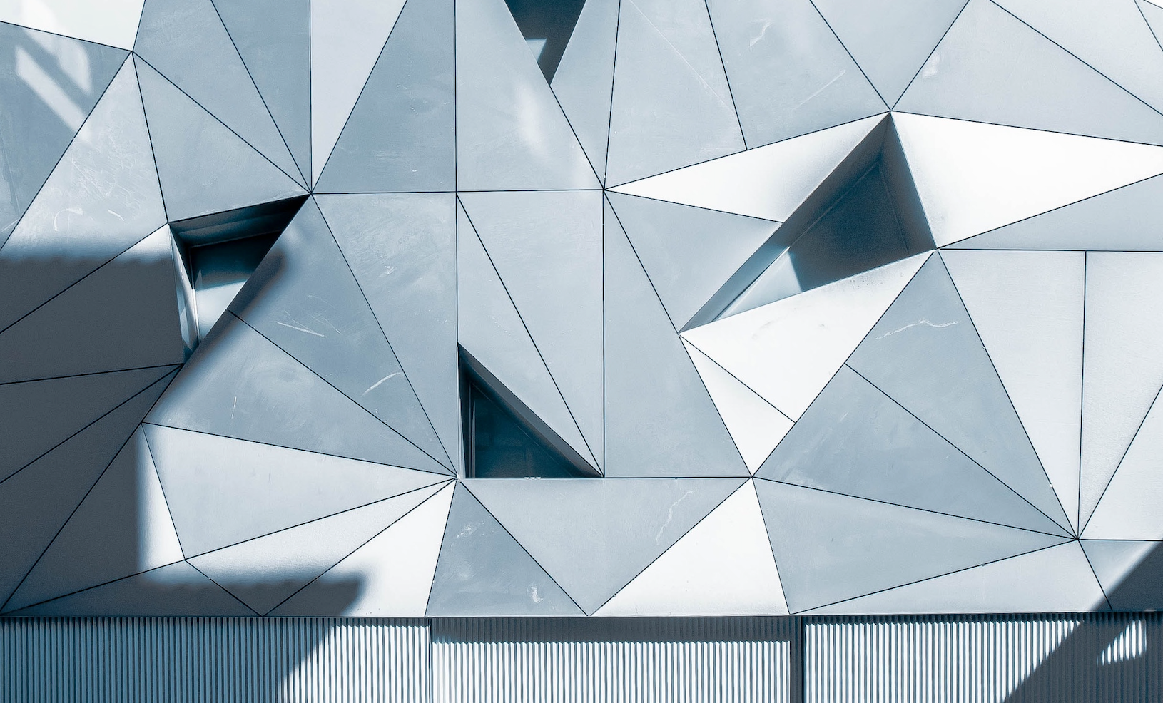 Abstrakt arkitektur med mange trekanter i grå og hvite nyanser, og mørke skygger.