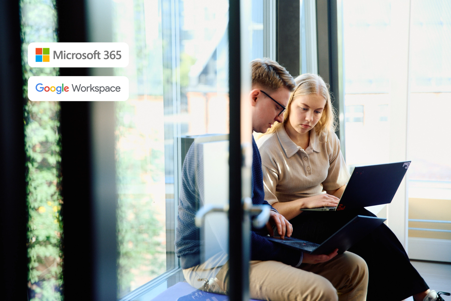 To studenter sitter ved et stort vindu med hver sin bærbare datamaskin, med logoer for Microsoft 365 og Google Workspace.