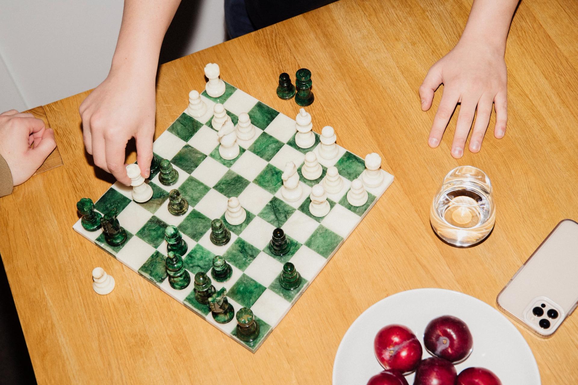 En person flytter en sjakkbrikke på et marmorbrett, med en tallerken plommer og en telefon på bordet.