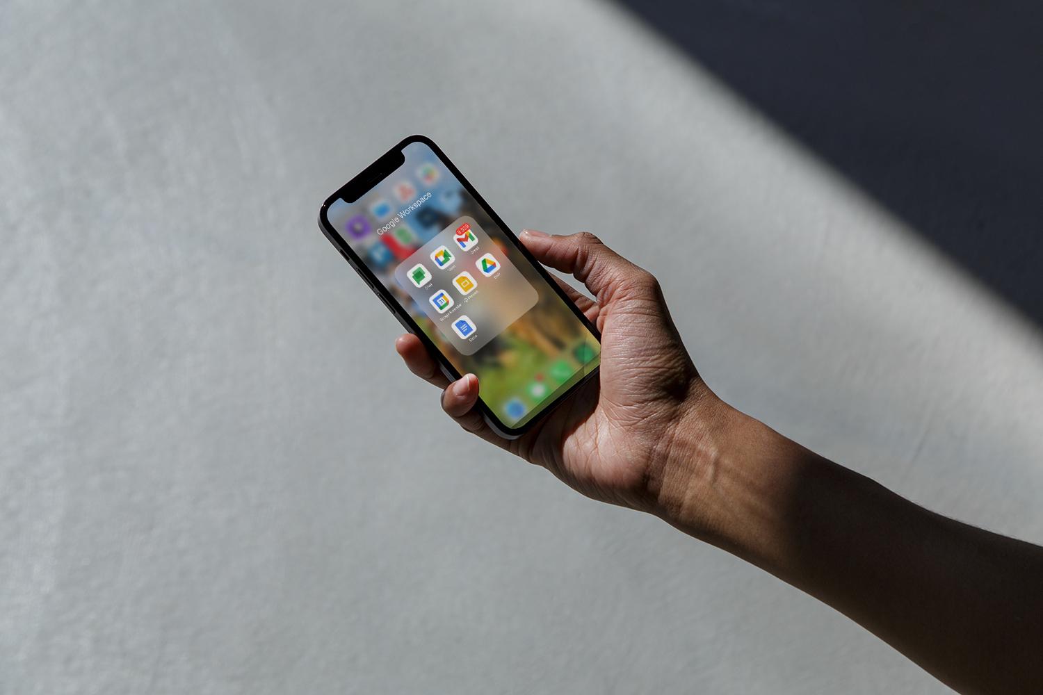 En hånd holder en smarttelefon som viser Google Workspace-apper.