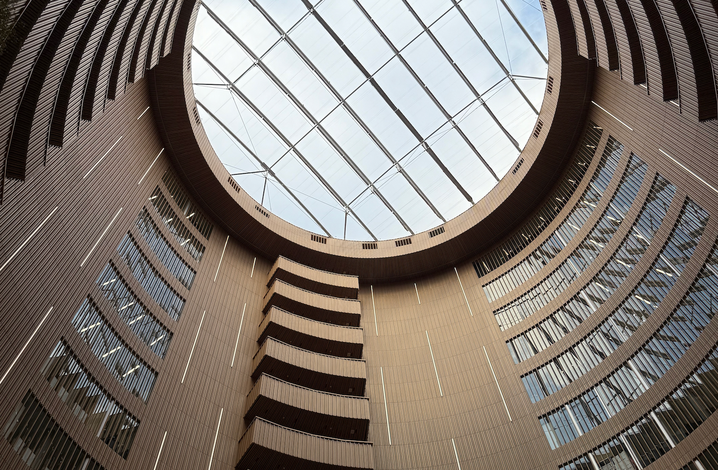 Imponerende, sirkulært atrium med treribber, store vindusflater og glasstak, sett nedenfra.