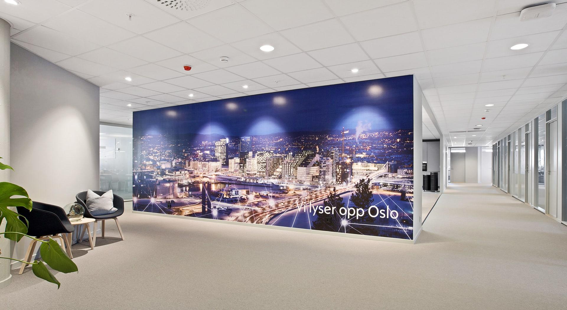 Moderne kontorkorridor med veggbilde av Oslo om natten og sittegruppe.