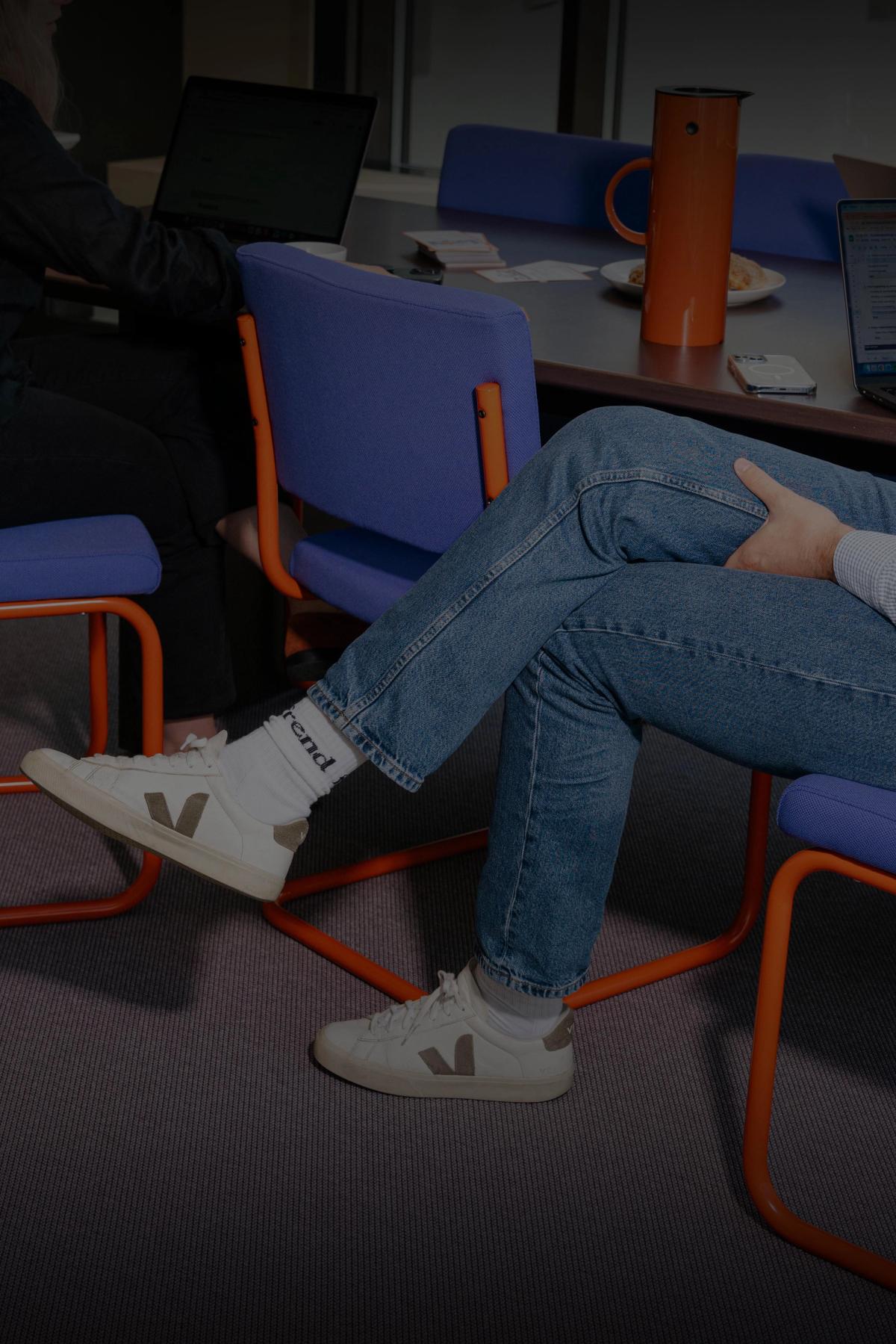 To personer sitter ved et møtebord med bærbare datamaskiner, et brett med boller og en termokanne.