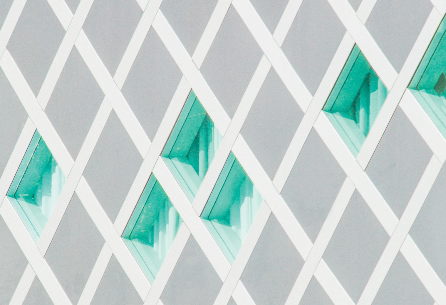Grå vegg med et diagonalt rutenett av hvite bånd og noen smale, rombeformede vinduer med grønn farge.