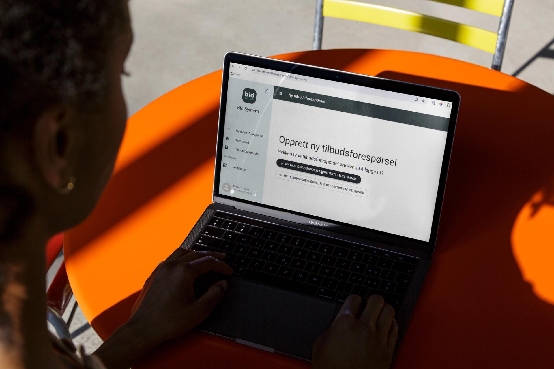 En person bruker en bærbar PC på et oransje bord for å opprette en ny tilbudsforespørsel.