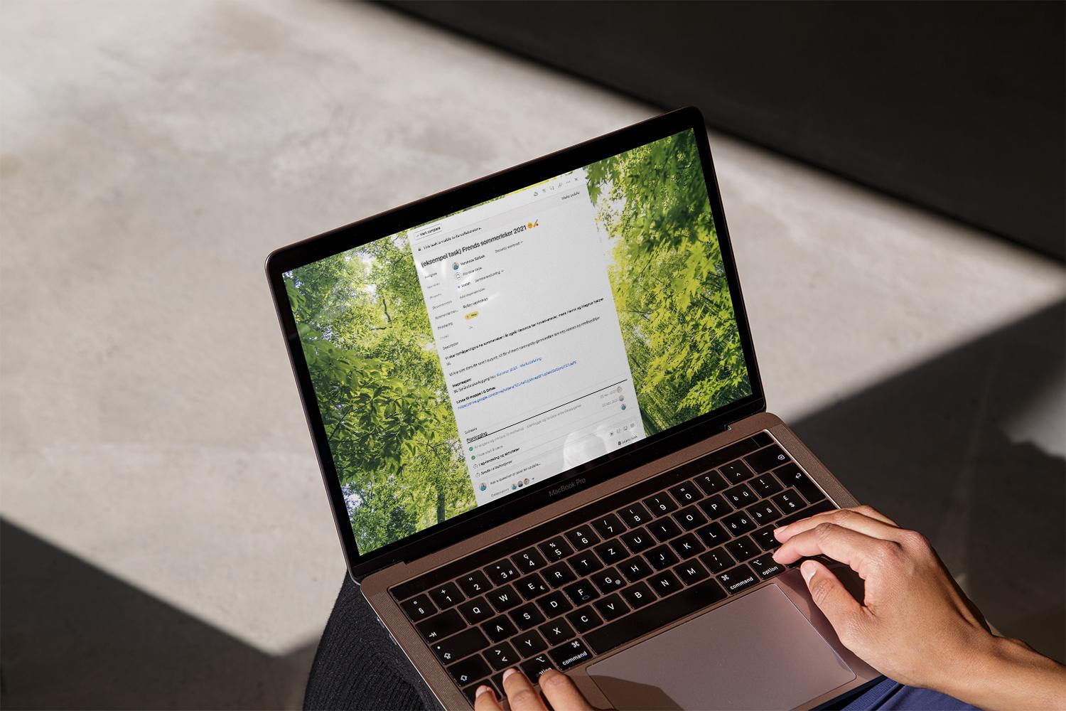En person bruker en MacBook Pro til å se en Trello-oppgave med grønne trær som bakgrunn.