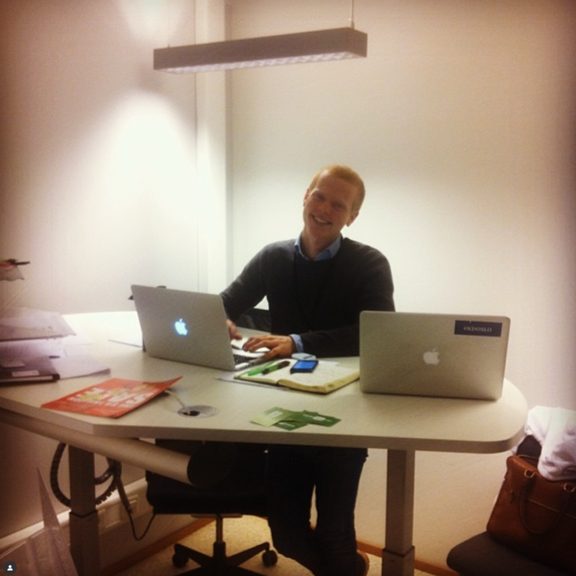 En smilende mann med laptoper på et bord, arbeider på et kontor.