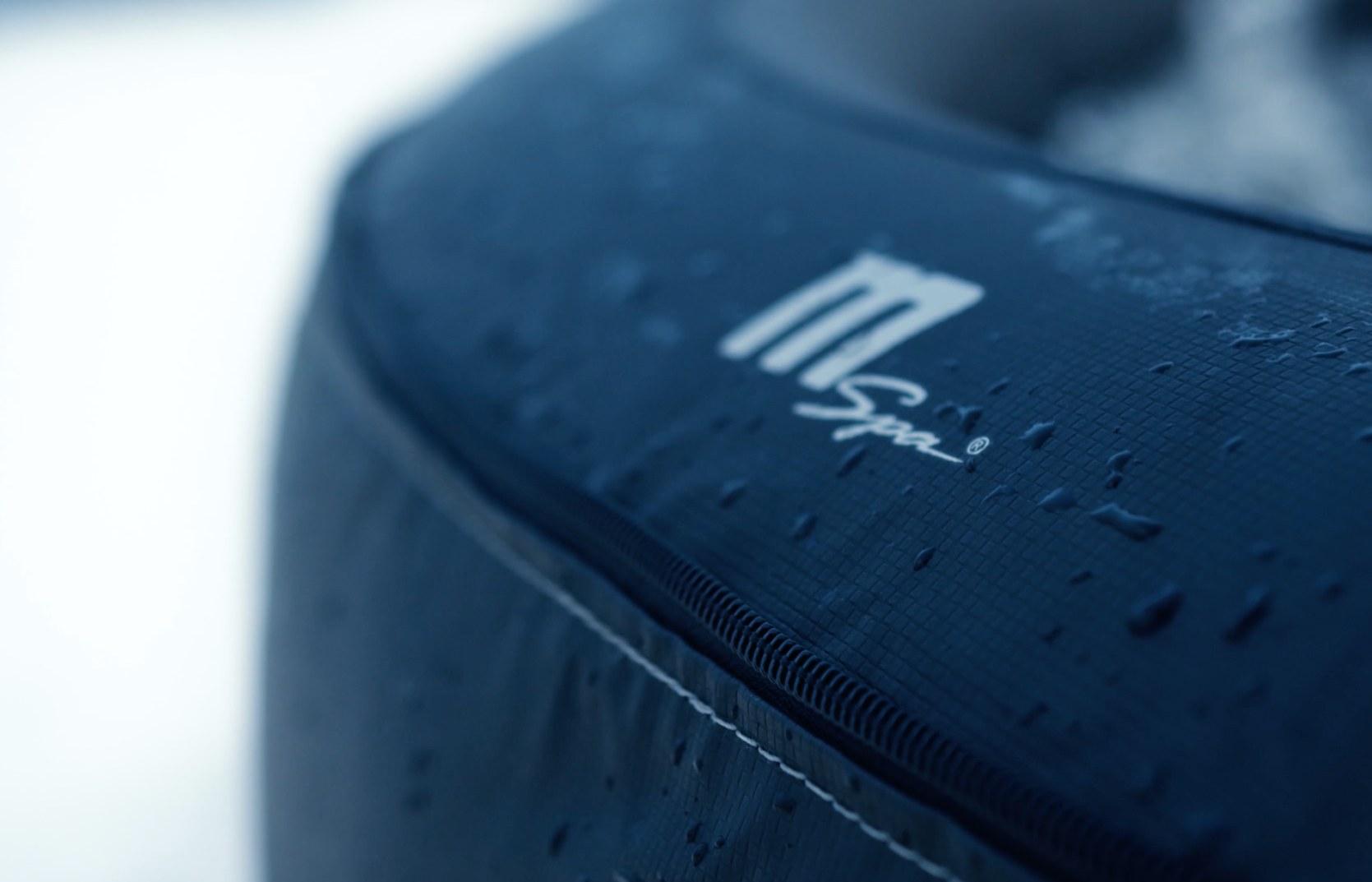 Nærbilde av en mørkeblå, vanndråpedekket overflate med en hvit "M Spa" logo og en glidelås.