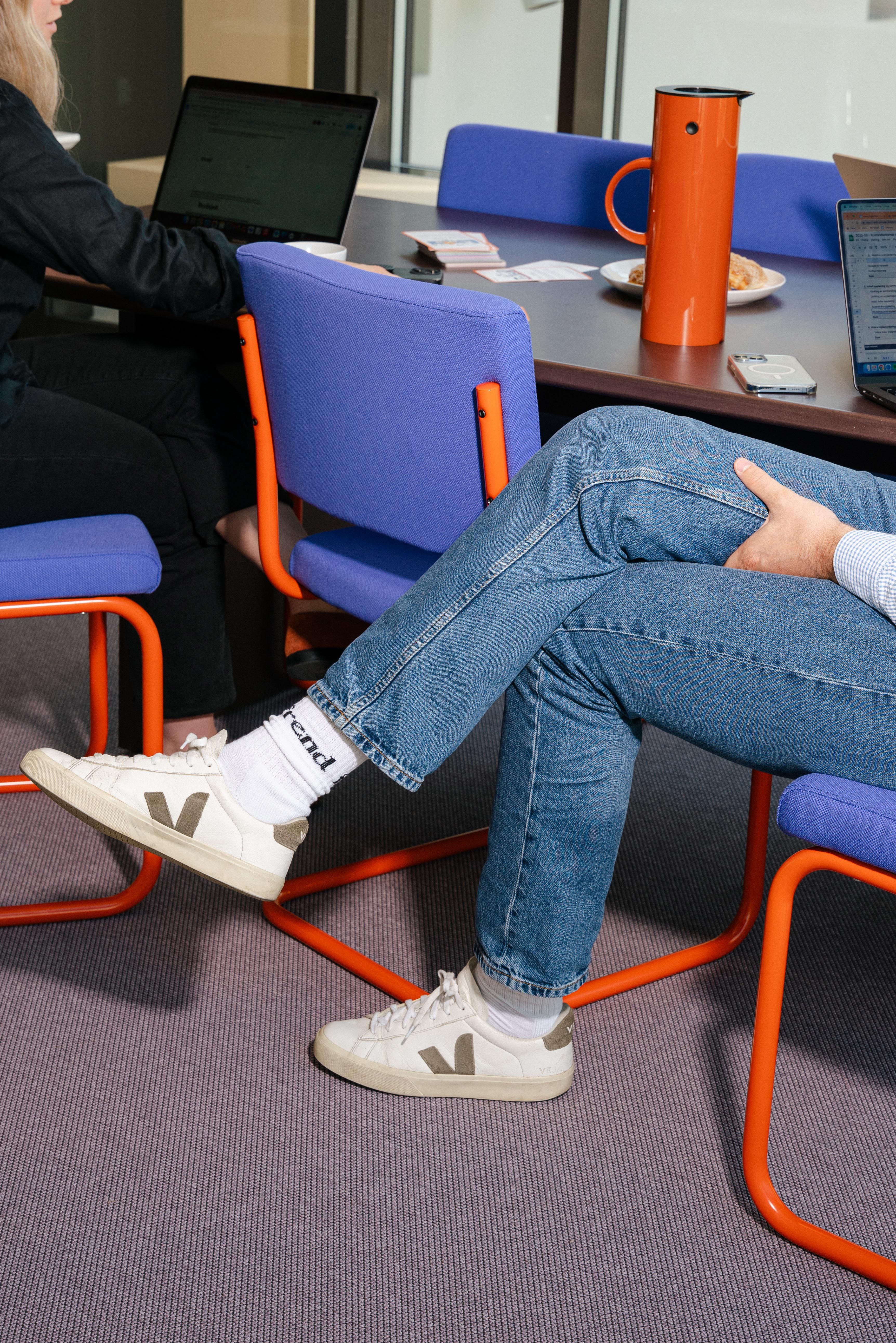 To personer sitter ved et møtebord med bærbare datamaskiner, en termokanne og brosjyrer.