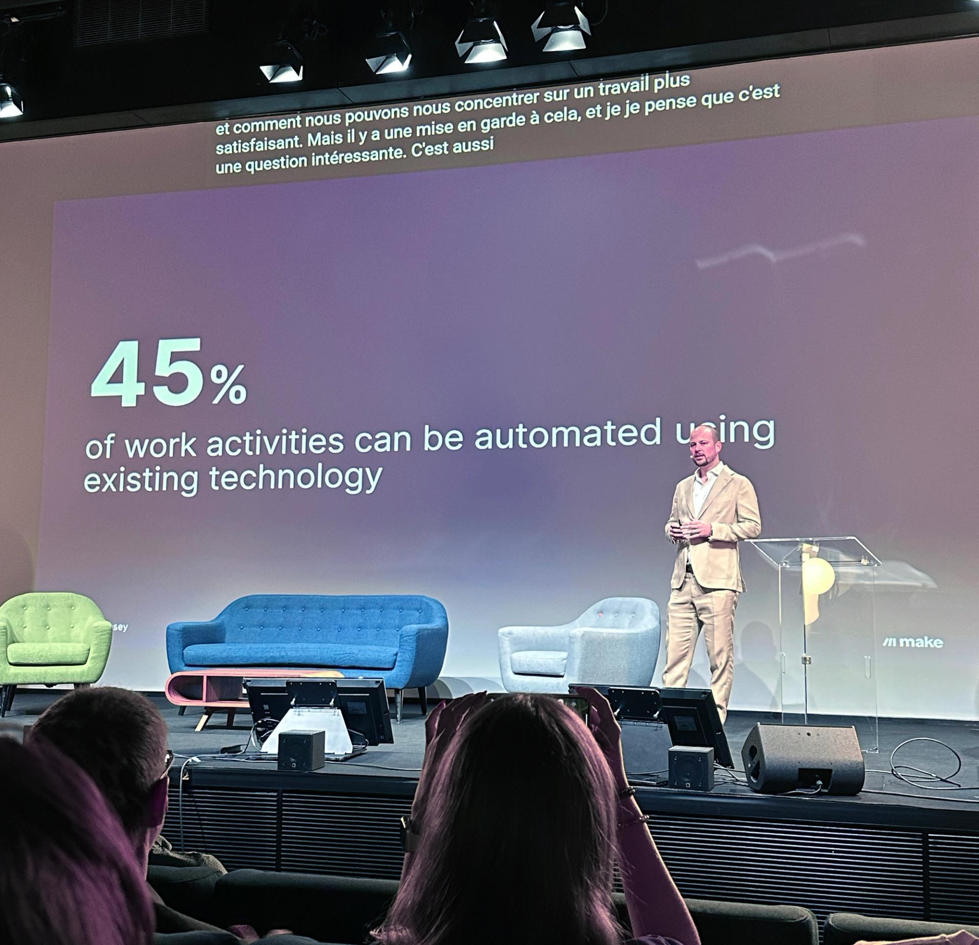 En mann presenterer på en scene med teksten "45% av arbeidsaktiviteter kan automatiseres med eksisterende teknologi" og publikum observerer.