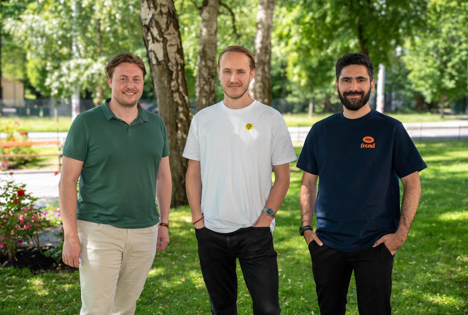 Three men standing outdoors on grass, with trees in the background. They are casually dressed and smiling at the camera.