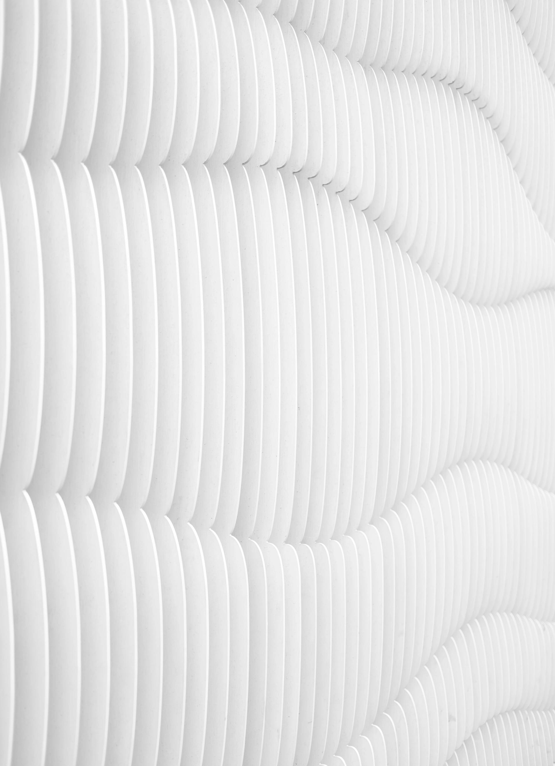 Hvit vegg med vertikale lameller som bølger seg diagonalt og danner et tredimensjonalt mønster.