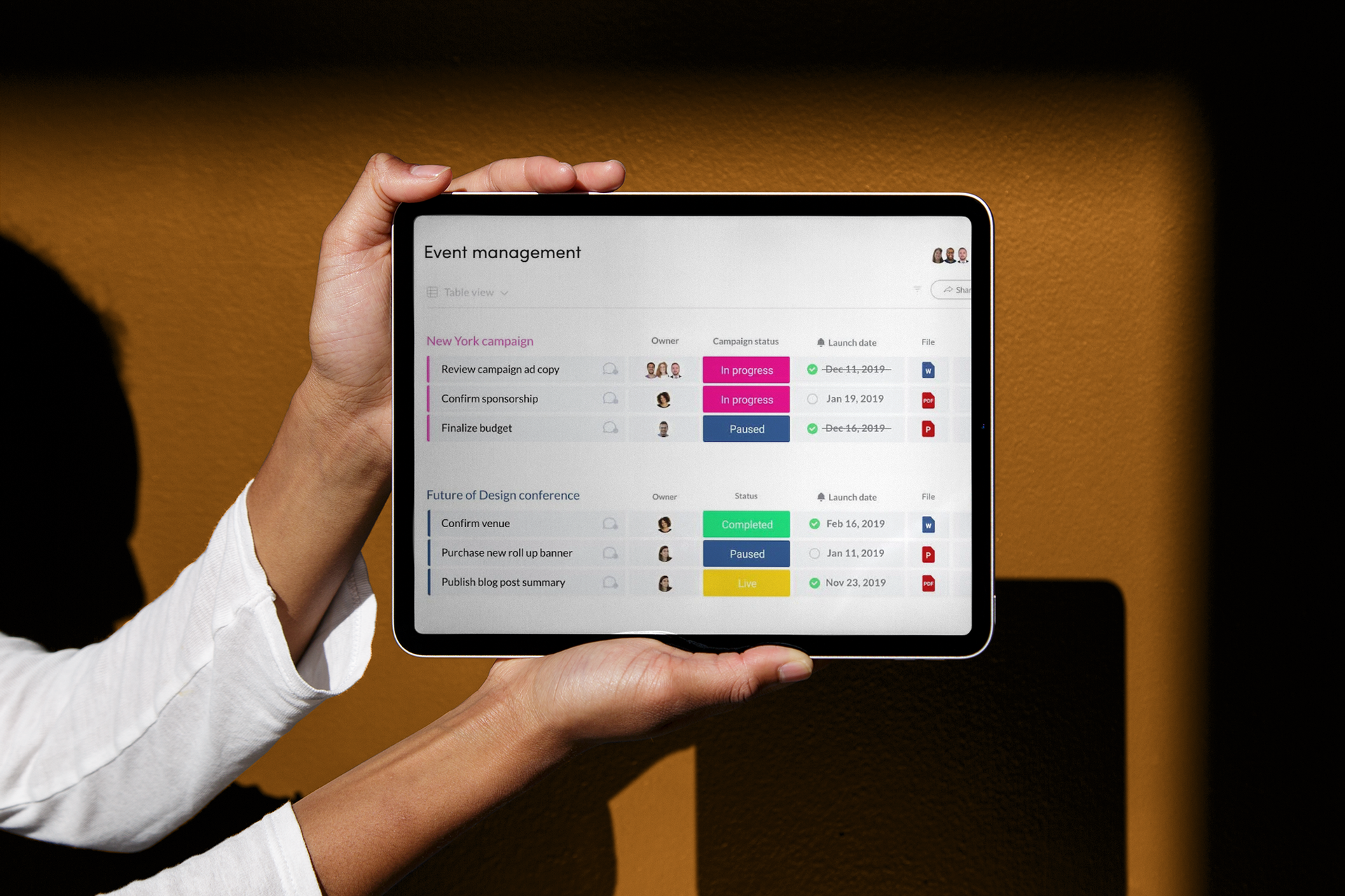 En person holder et nettbrett med en applikasjon for arrangementstyring, som viser status for ulike oppgaver.