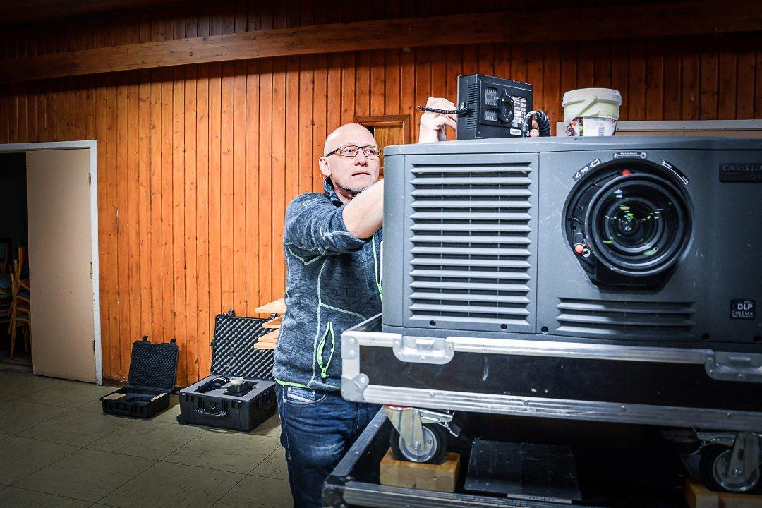 Mann kobler til en moderne DLP-kinoprojektor i et rom med trepanelvegger.