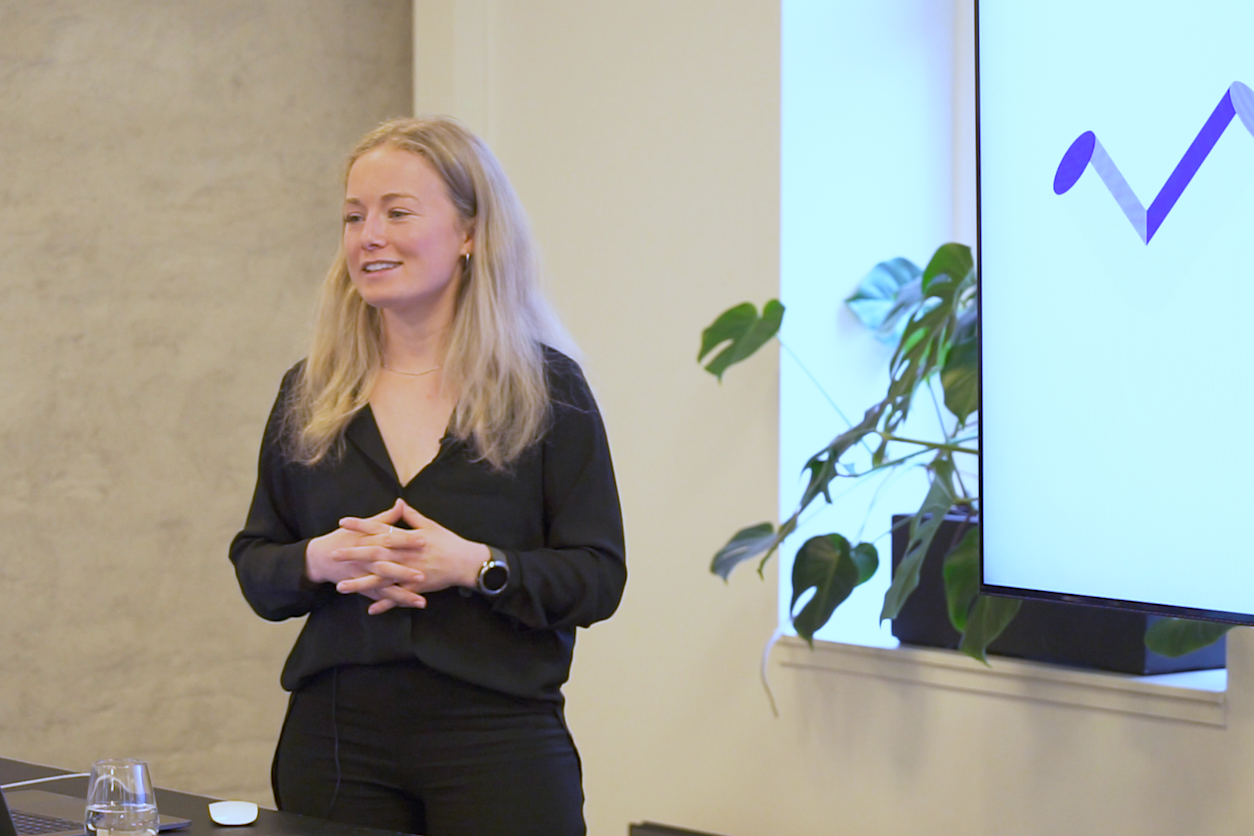 Kvinne med blondt hår presenterer prosjekt- og prosessledelse i Teams, med grafikk på en storskjerm og en laptop på bordet.